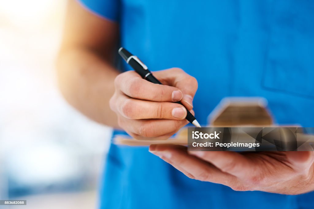 I'll have to put that on record Cropped shot of a male nurse writing something on a clipboard Note Pad Stock Photo