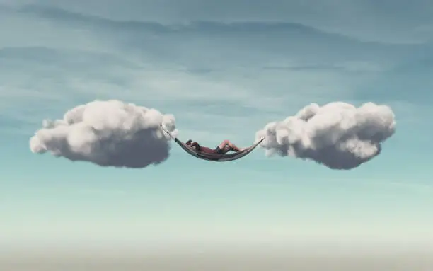 Photo of Young man relaxes in a hammock between two clouds.