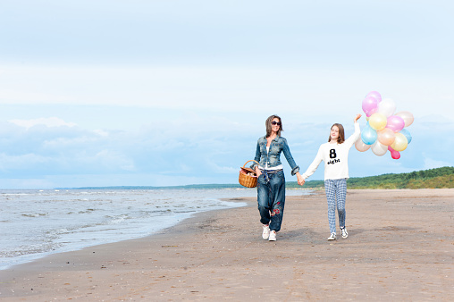 Mother and daughter together holding hands and walking along the beach. Summertime outdoors horizontal vibrant colored image.