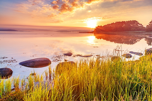 Breathtaking sunrise scenery, View at Sweden coastline covered with green grass over Northern Sea at dramatic dusk sky and sun touched horizon. Wallpaper landscape in red - green - orange color tones.