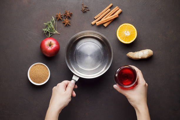Hands cook mulled wine from ingredients on brown table.