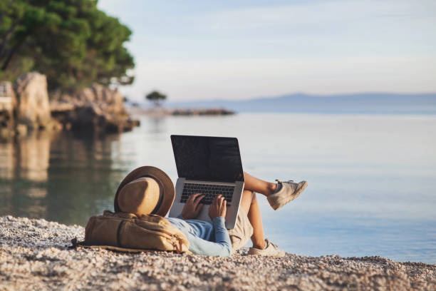 giovane donna che usa laptop su una spiaggia - vacations holiday internet summer foto e immagini stock