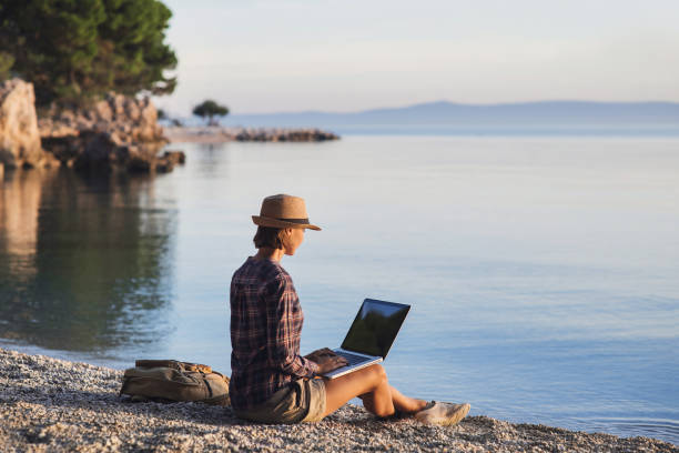 istock Young woman using laptop near the sea 883731494