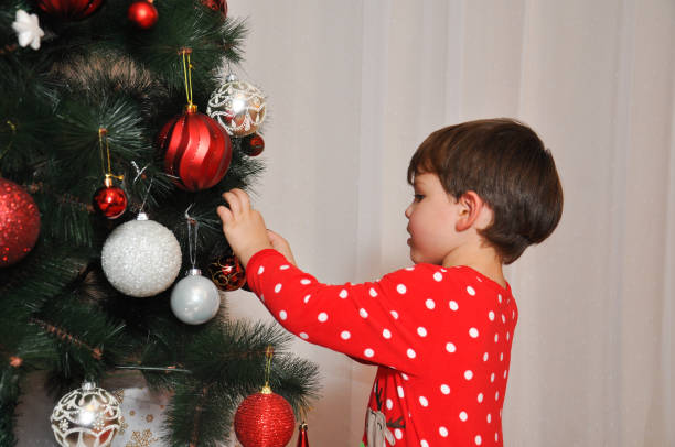 istock Boy in New Year's pajama decorating Christmas tree. 883732098