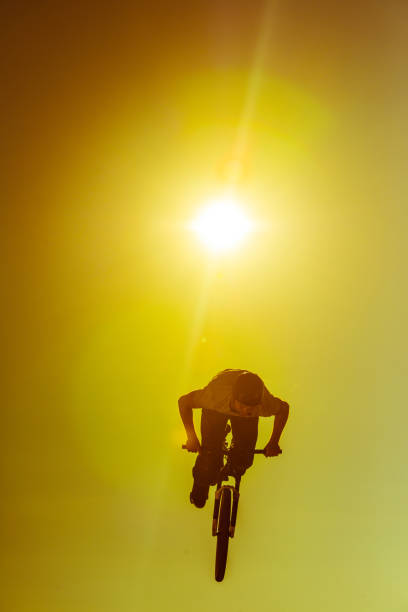 Man with dirt jump bike in air against sky while enjoying dirt jumping sport during sunset.