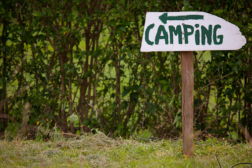 A wooden camping hand painted sign with the arrow pointing to the left