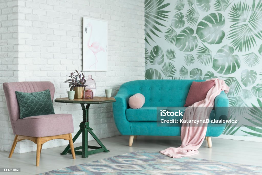 Pink chair and blue sofa Green table with plant between pink chair and blue sofa in floral living room with wallpaper and poster Wallpaper - Decor Stock Photo