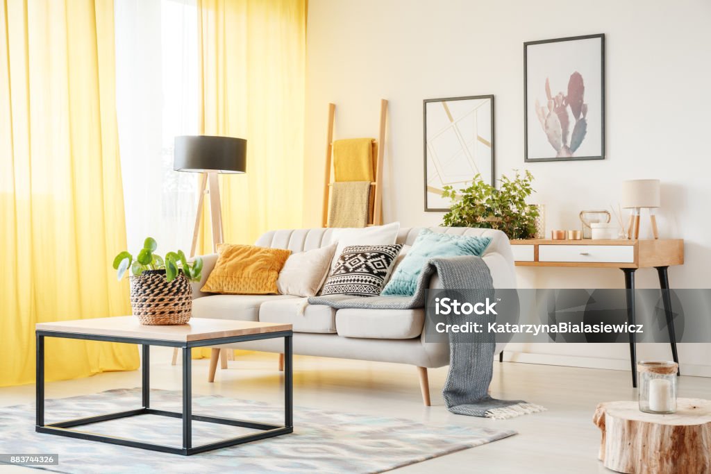 Plant in warm living room Plant on table and lamp in warm living room with yellow curtains, posters and pillows on sofa Yellow Stock Photo