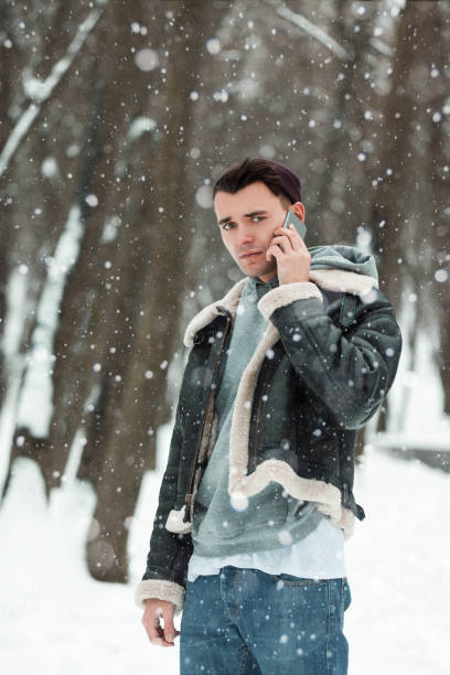 istock a young guy holding a phone. winter background 883755048