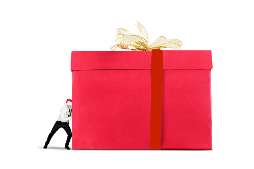 Young Caucasian businessman wearing Santa hat and pushing a big Christmas gift, isolated on white background