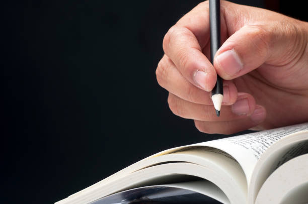 istock Close-up of hand holding pencil and reading book. 883761726