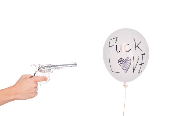cropped shot of hand holding revolver and shooting balloon with fuck love inscription isolated on white
