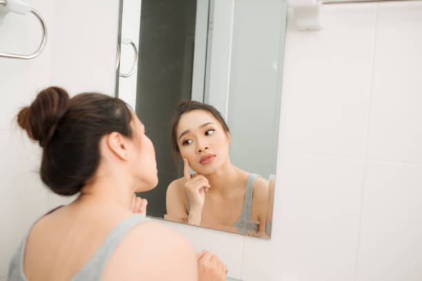 istock Asian woman holding a mirror, touch and worrying about her face 883793056