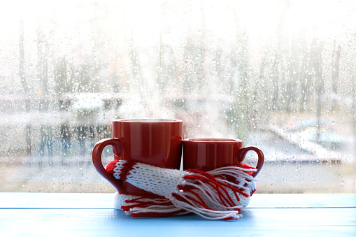 big and small red cup wrapped in a scarf on window background with drops after the rain