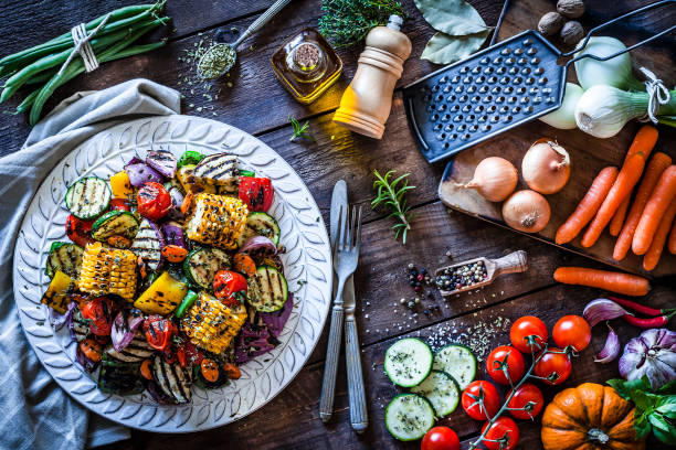 Grilled vegetables plate shot from above on rustic wooden kitchen table Grilled vegetables plate shot from above on rustic wooden kitchen table. The plate is on a gray textile napkin at the left of an horizontal frame and some fresh vegetables are at the right. DSRL studio photo taken with Canon EOS 5D Mk II and Canon EF 100mm f/2.8L Macro IS USM side dish stock pictures, royalty-free photos & images
