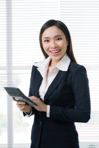 istock Smiling asian businesswoman in bright office using calculator 883802560
