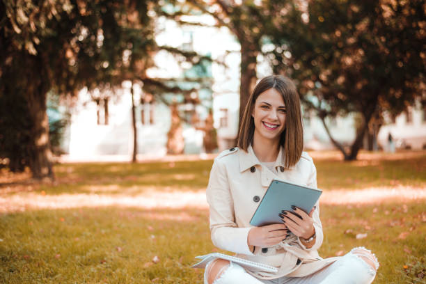 istock Happy young woman with digital tablet sitting on grass in park. 883808566