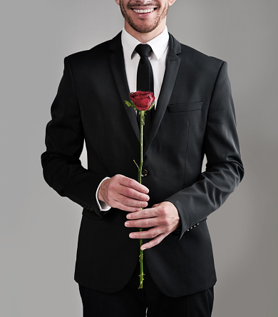 Studio shot of a well-dressed man holding a red rose against a gray background