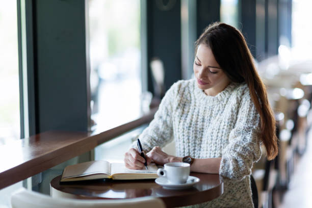 istock Young attractive woman writing diary in cafe 883832814