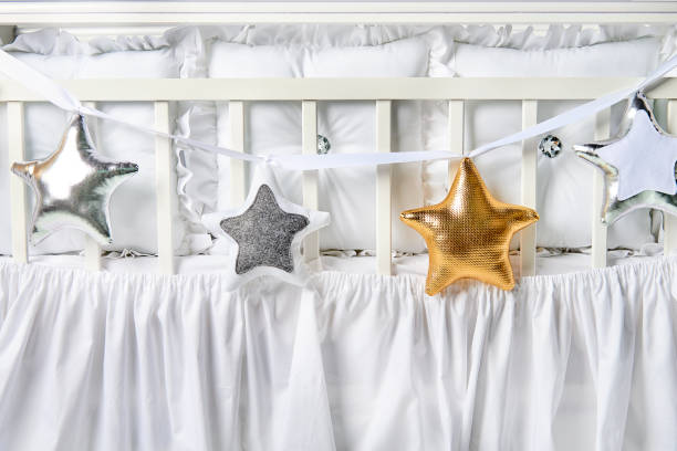 istock Silver, gold and white star shaped pillows on a white baby cot 883839476