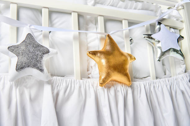 istock Silver, gold and white star shaped pillows on a white baby cot 883839520