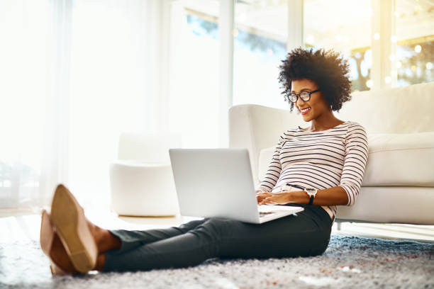 Just another day working in my own personal home office Shot of a cheerful young woman doing online shopping on her laptop while being seated on the floor at home woman lifestyle stock pictures, royalty-free photos & images