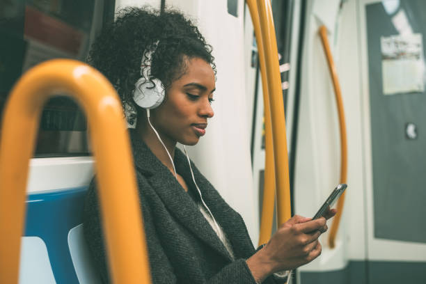 Happy young black woman sitting inside the underground listening to music "n stock photo