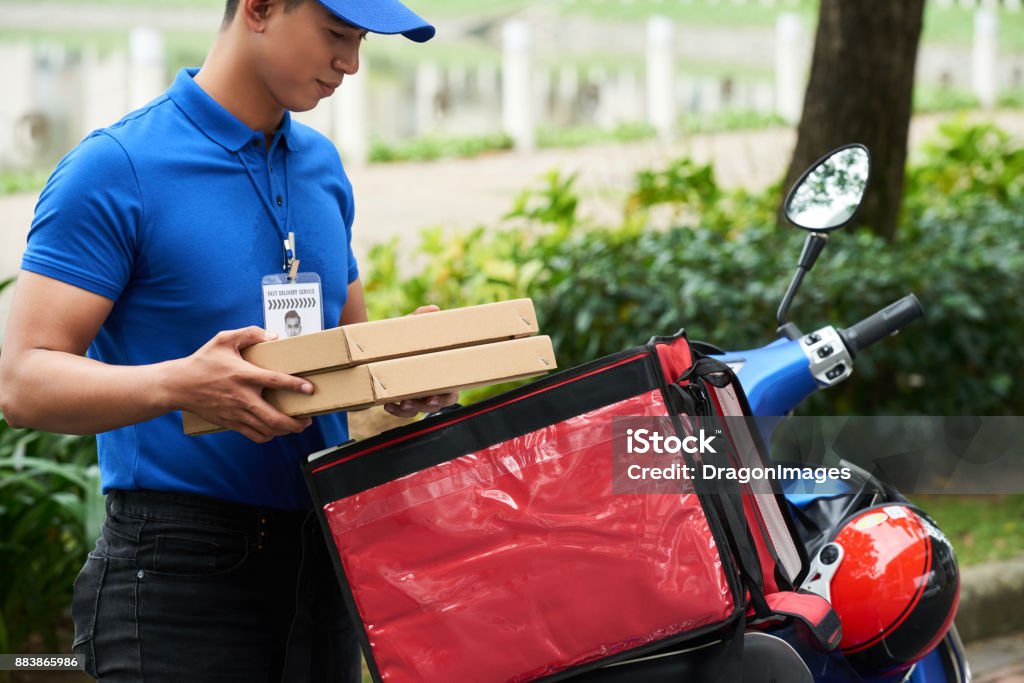 Food courier Vietnamese courier putting pizza packages into bag on scooter Delivering Stock Photo