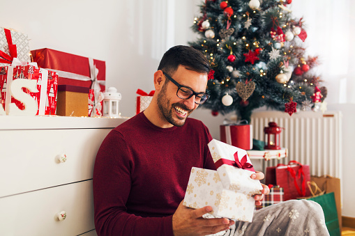 Smiling young man opening Christmas gift at home
