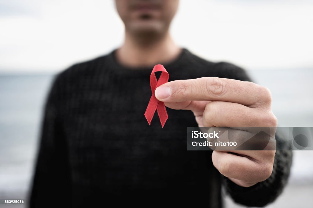 man with red ribbon for the fight against AIDS closeup of a young man with a red awareness ribbon for the fight against AIDS in his hand HIV Stock Photo