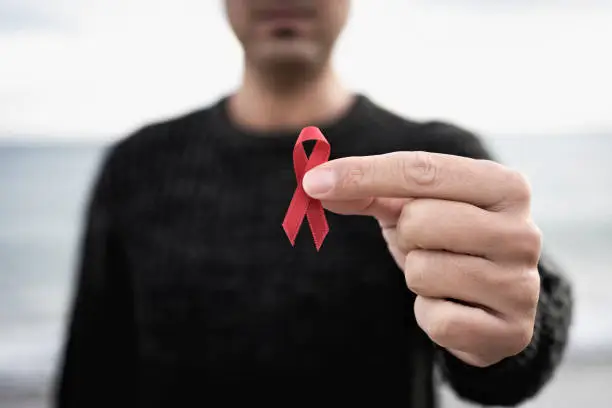 closeup of a young man with a red awareness ribbon for the fight against AIDS in his hand