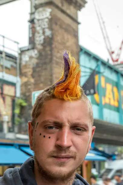 Photo of London Punk scene, one Punk Male with crested hairstyle, in the back the Camden Lock sign at the entrance of Camden market.