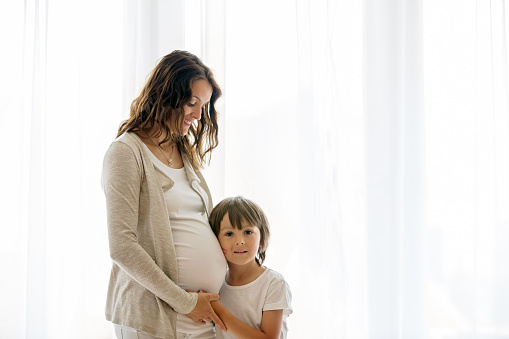 Portrait of beautiful pregnant woman and her cute child, isolated image on white background, back lit