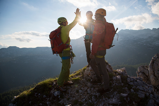 Hikers giving high-five while celebrating success on top of mountain, hikers carrying rucksack and wearing sports helmet.