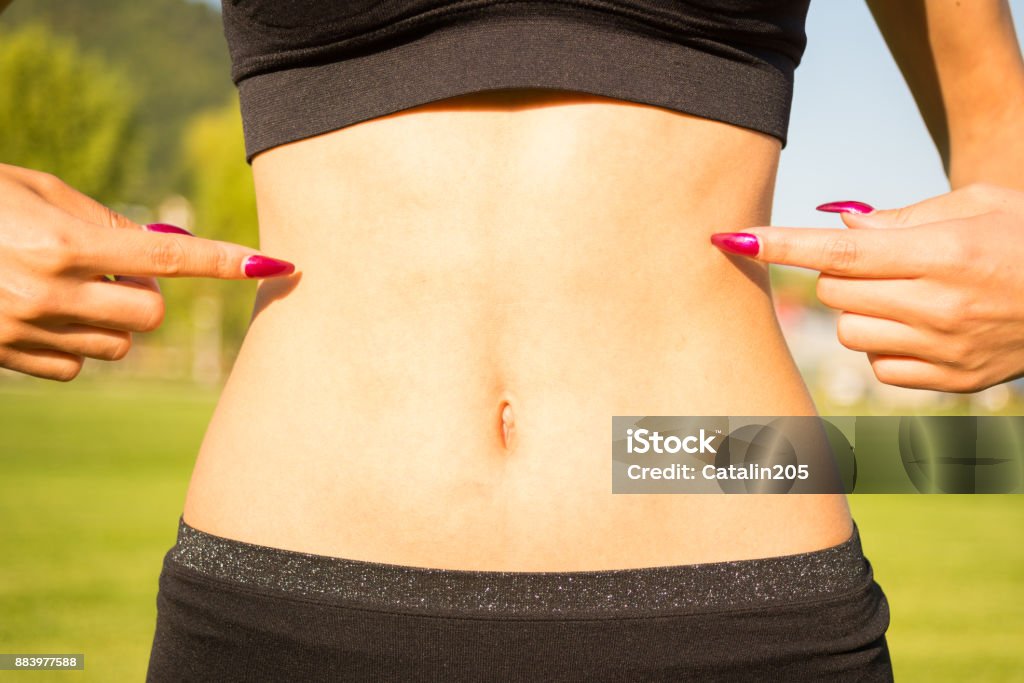 Closeup of woman pointing finger at her tummy Closeup of woman pointing finger at her well trained tummy outdoors Abdomen Stock Photo