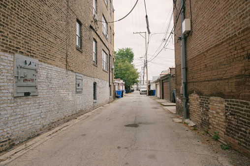 This is a horizontal color photograph of an urban Midwest Chicago Illinois Brick Lined Residential Street Alley Background. There are no people, photoraphed on an overcast day with a wide angle perspective and vanishing point.
