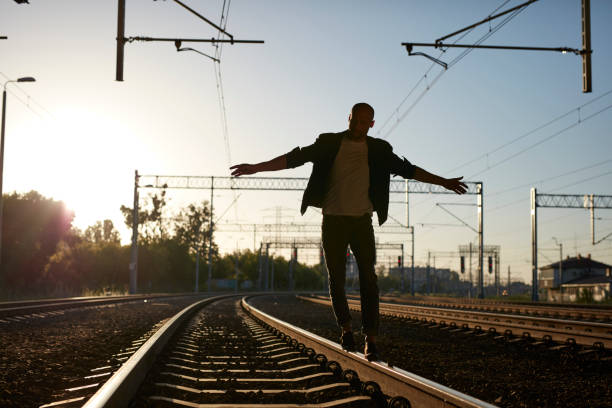 Outsider walking on roilroad track in front of camera. Open arms.