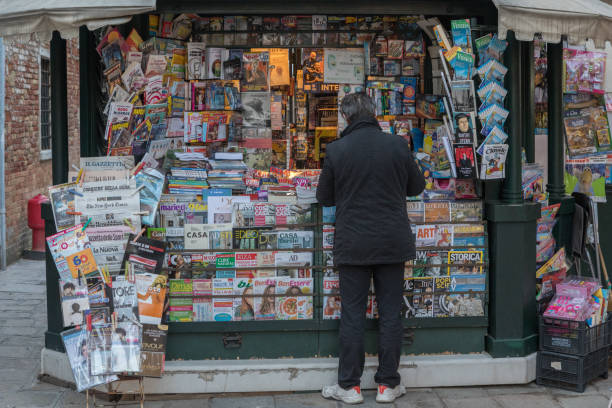 An Italian man buying a newspaper from a magazine store in rio terà barba frutariol, Venice which is a city in northeastern Italy and the capital of the Veneto region.