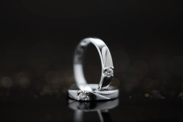 primo piano paio di fedi nuziali in platino con diamante su sfondo riflesso bokeh - jewelry gem gold reflection foto e immagini stock