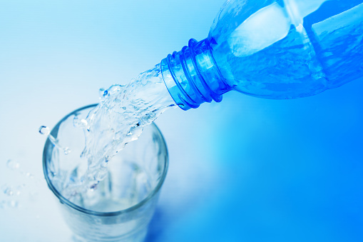 Close up shot : Pour water from plastic bottle in to the glass on blue backgroud