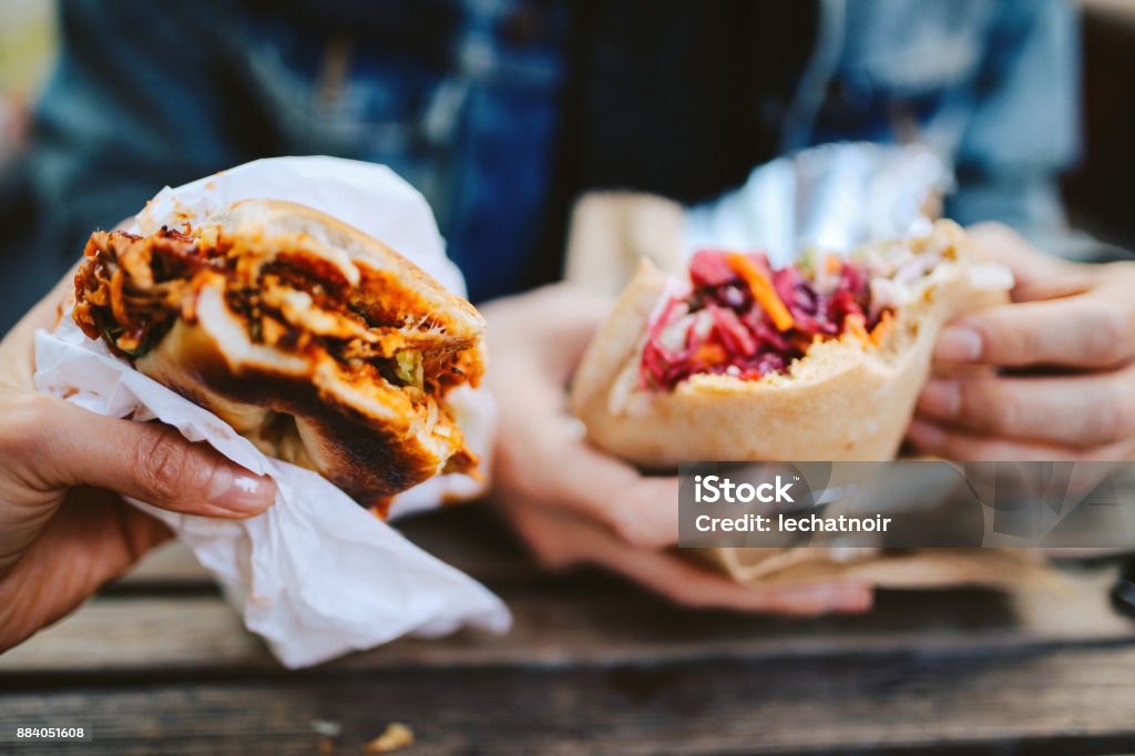 Close up of a Texas pulled pork bbq burger and a falafel outdoors Close up image of two people eating a Texas style pulled pork barbeque and a falafel fast food in East London. Hand Stock Photo