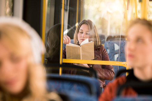 selective focus of young woman reading book in city bus