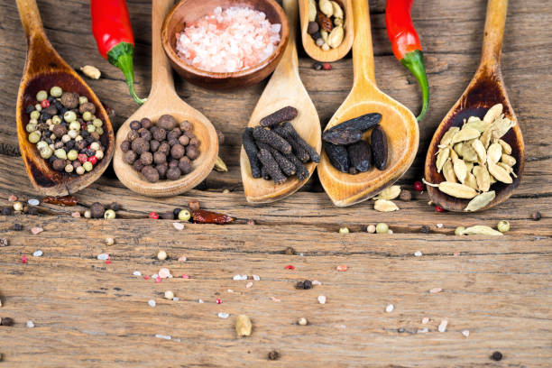 close-up of five wooden cooking spoons with various exotic spices and two red chili peppers and a wooden bowl with pink crystal salt on a rustic wooden background and copy space - salt crystal spoon food imagens e fotografias de stock