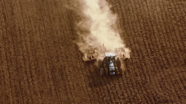 AERIAL Tractor driving across a vast field in sunshine