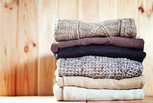 Knit cozy sweater folded in a pile on wooden background .Warm the concept. Copyspace.