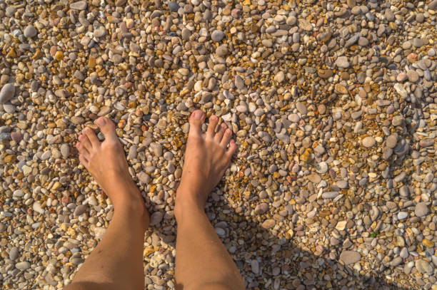 istock Woman's feet standing on small pebbles and sand. Space for text 884087162
