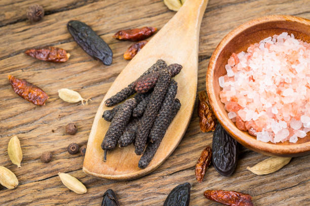 closeup of indian long pepper on a wooden cooking spoon and pink crystal salt in a small wooden cup on rustic wood background - salt crystal spoon food imagens e fotografias de stock