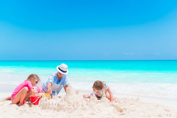 istock Father and little daughters making sand castle at tropical beach 884122296