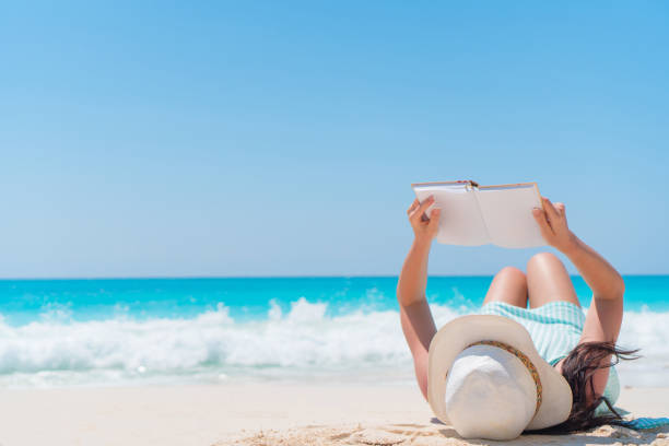 istock Young woman reading book lying tropical white beach 884122510