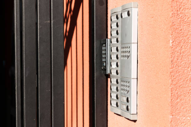 istock Sideview of modern intercom with security dials and buttons for bells on the building exterior wall with metal secutity gate selective focus 884148440